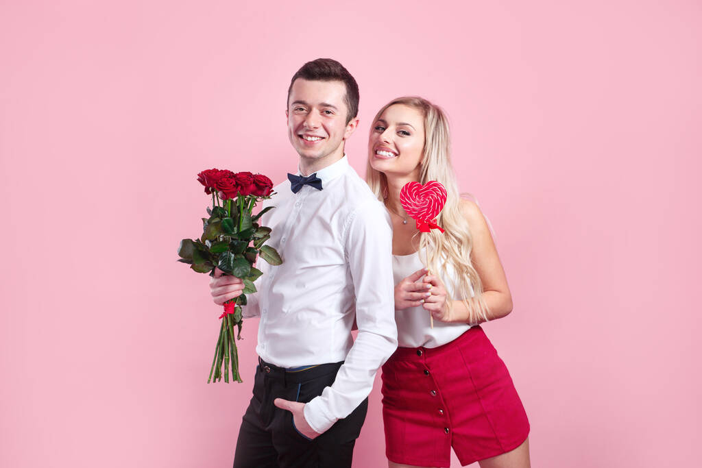 З Днем святого Валентина. Прекрасна романтична пара з квітами і червоним серцем на рожевому фоні.. - Фото, зображення