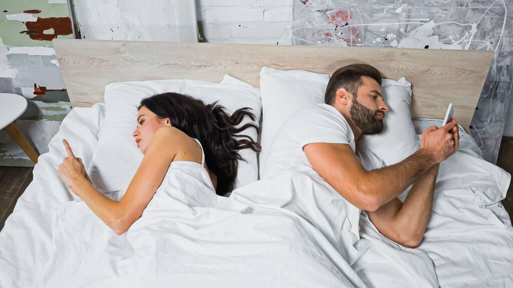 fiatal pár üzenetküldés okostelefonokon, miközben fekszenek az ágyban háttal - Fotó, kép