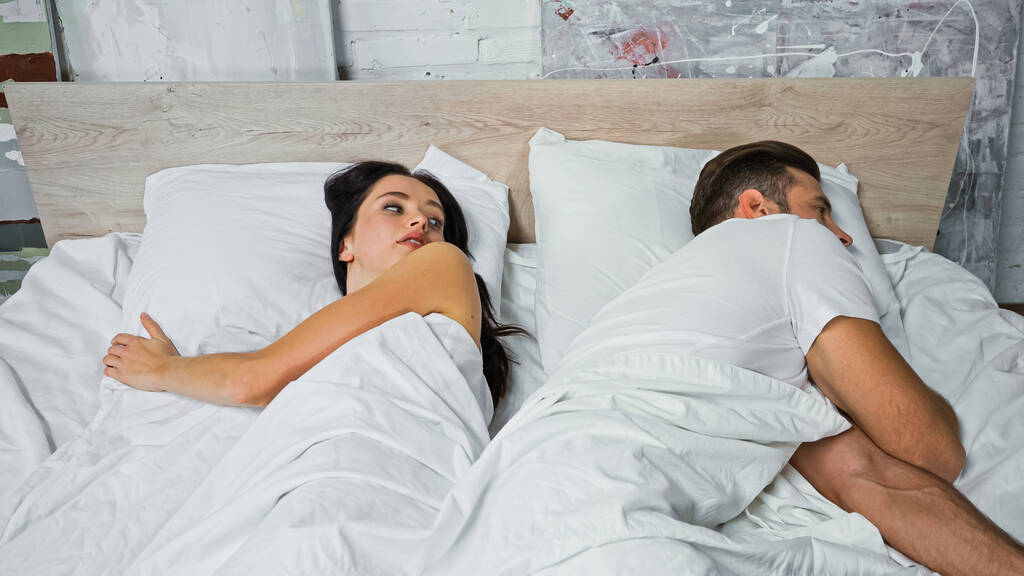 brunette woman looking at boyfriend lying nearby in bed - Photo, Image