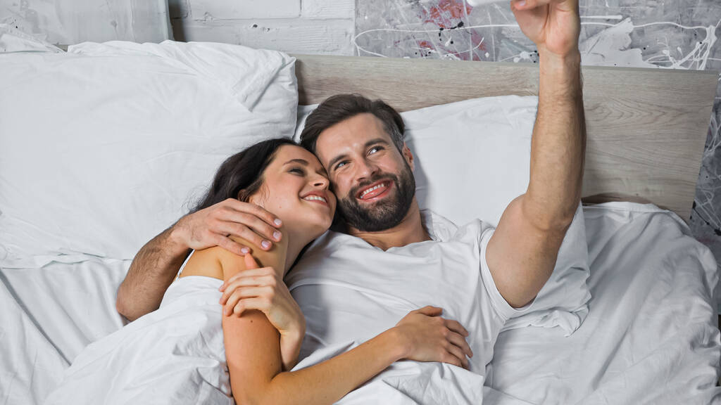 iloinen mies törröttää kielen kun makaa hymyilevä nainen sängyssä - Valokuva, kuva