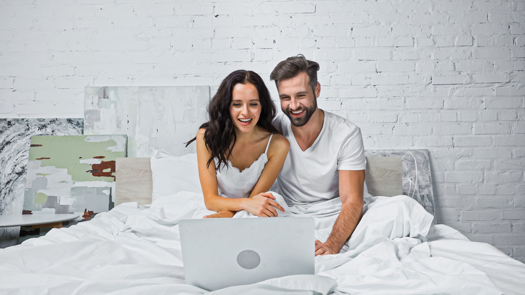 feliz joven pareja viendo comedia en el ordenador portátil en el dormitorio - Foto, imagen
