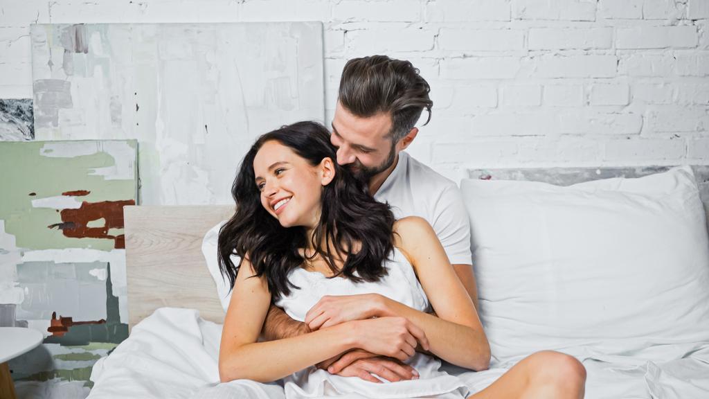 alegre joven pareja abrazándose mientras se divierten en la cama - Foto, Imagen