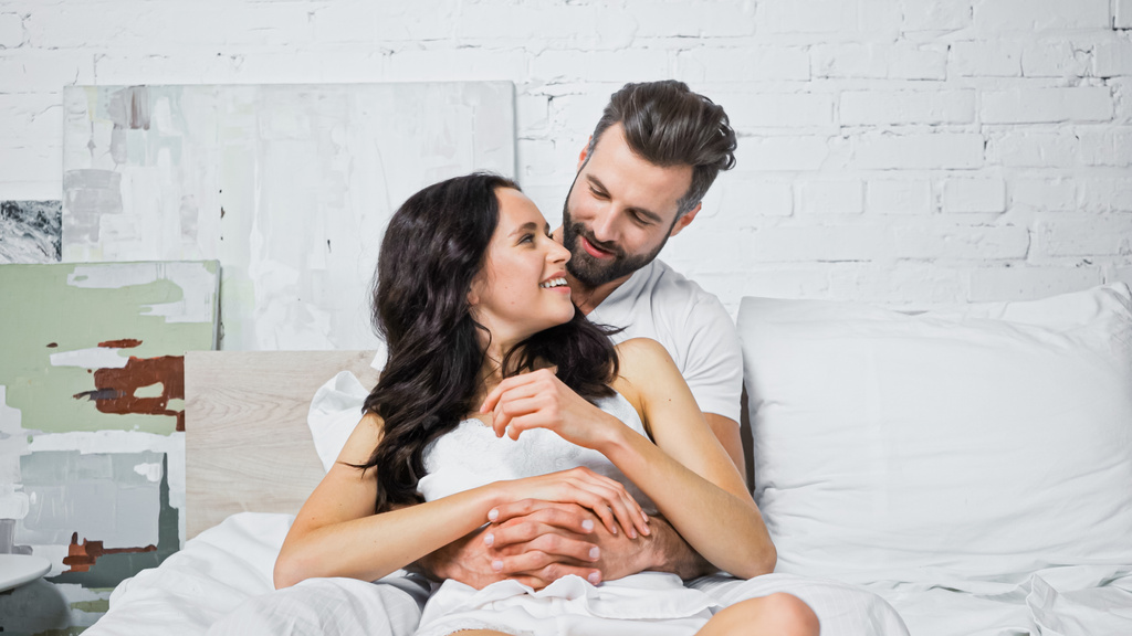 happy young couple looking at each other while having fun and hugging in bed - Photo, Image