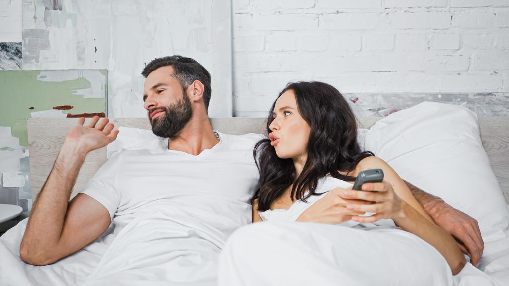brunette woman asking question to indifferent man while clicking tv channels with remote controller  - Photo, Image