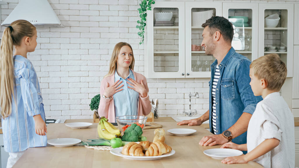 Ailesinin yanında duran bir kadın ve mutfak masasında yemek.  - Fotoğraf, Görsel
