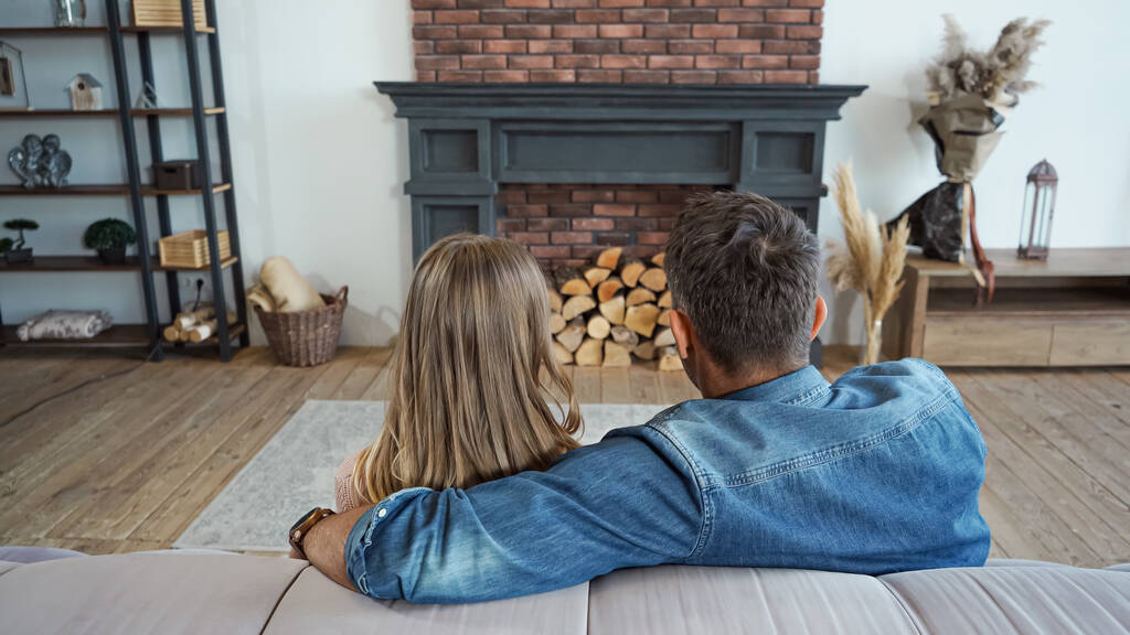 Back view of husband embracing wife near fireplace on blurred background at home  - Photo, Image