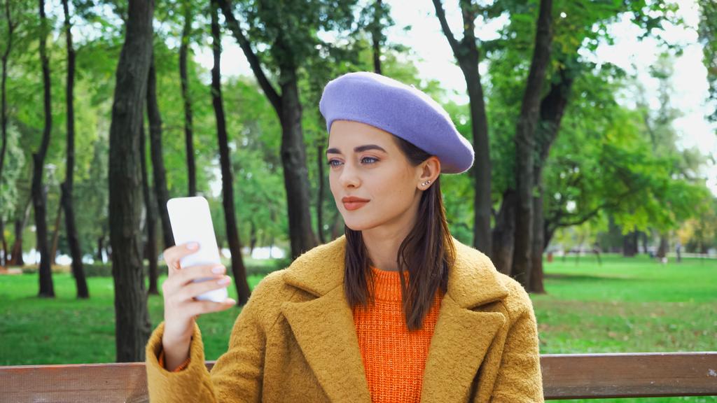 mladá žena ve stylovém podzimním oblečení zprávy na mobil v parku - Fotografie, Obrázek