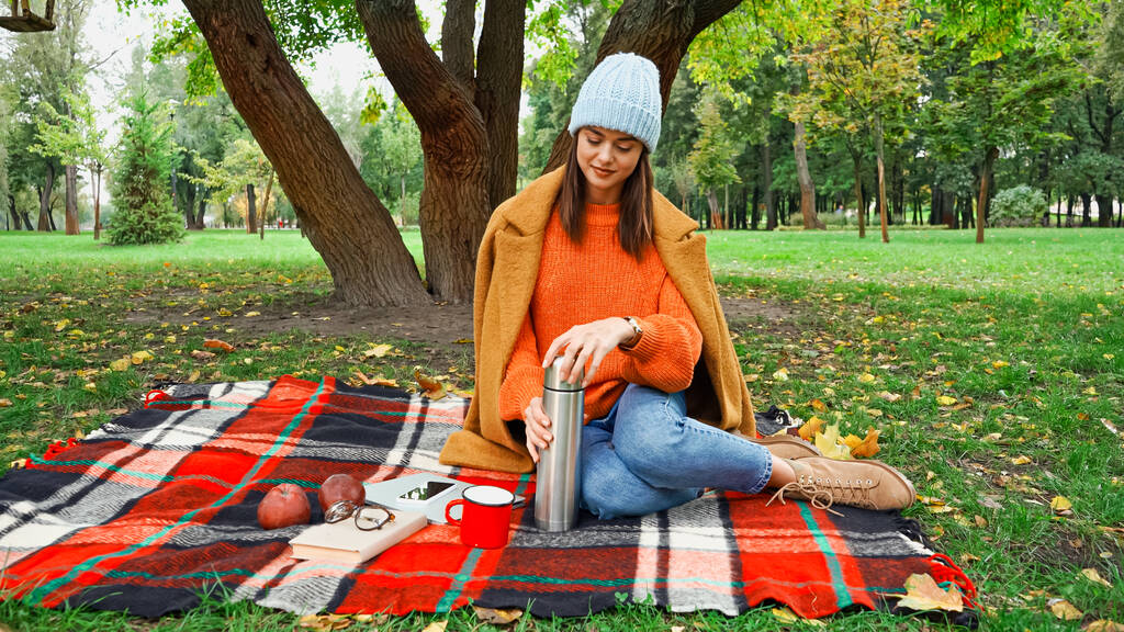 Parkta piknik yaparken termos açan şık sonbahar elbiseli bir kadın. - Fotoğraf, Görsel