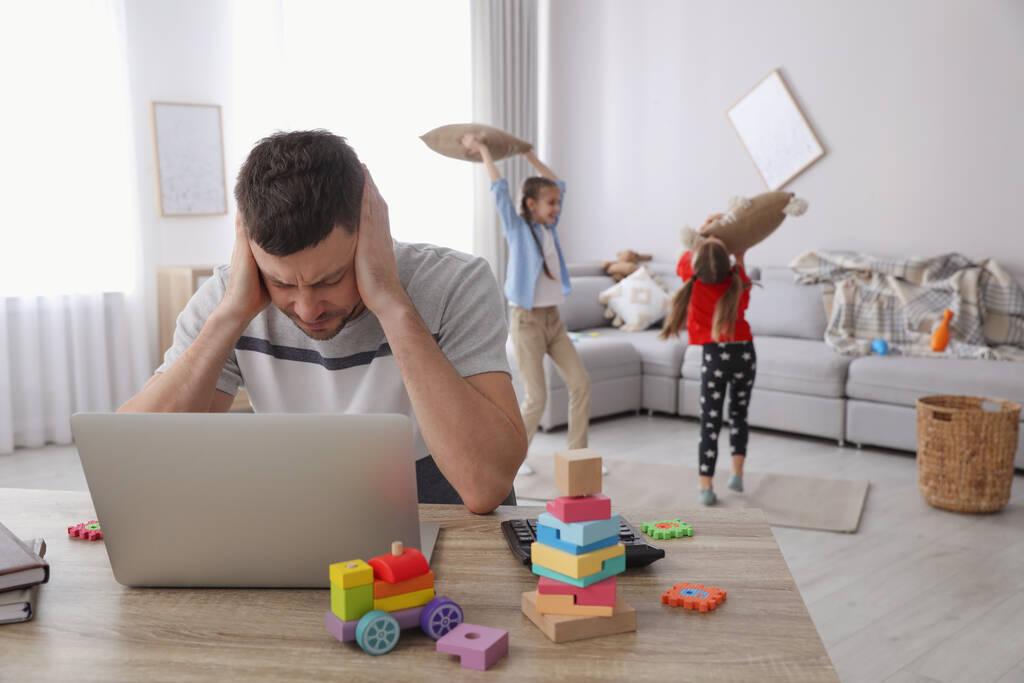 Kinderen storen gestresste man in de woonkamer. Werken vanuit huis tijdens quarantaine - Foto, afbeelding