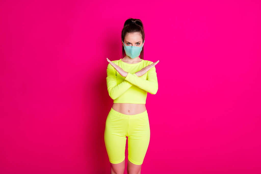 Retrato fotográfico de una mujer con máscara médica con las manos cruzadas mostrando un signo de prevención aislado sobre un fondo de color fucsia brillante - Foto, imagen