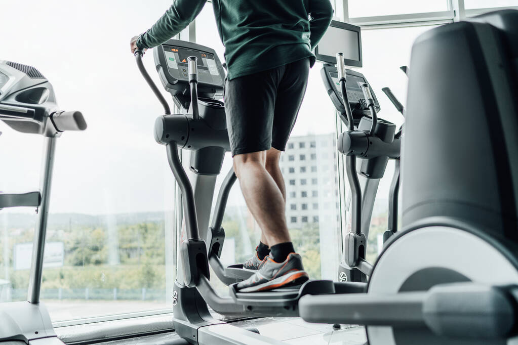 Cerrar el marco de las piernas masculinas en la máquina cardiovascular. Gimnasio, entrenamiento, estilo de vida saludable. Motivación, entrenador. - Foto, imagen
