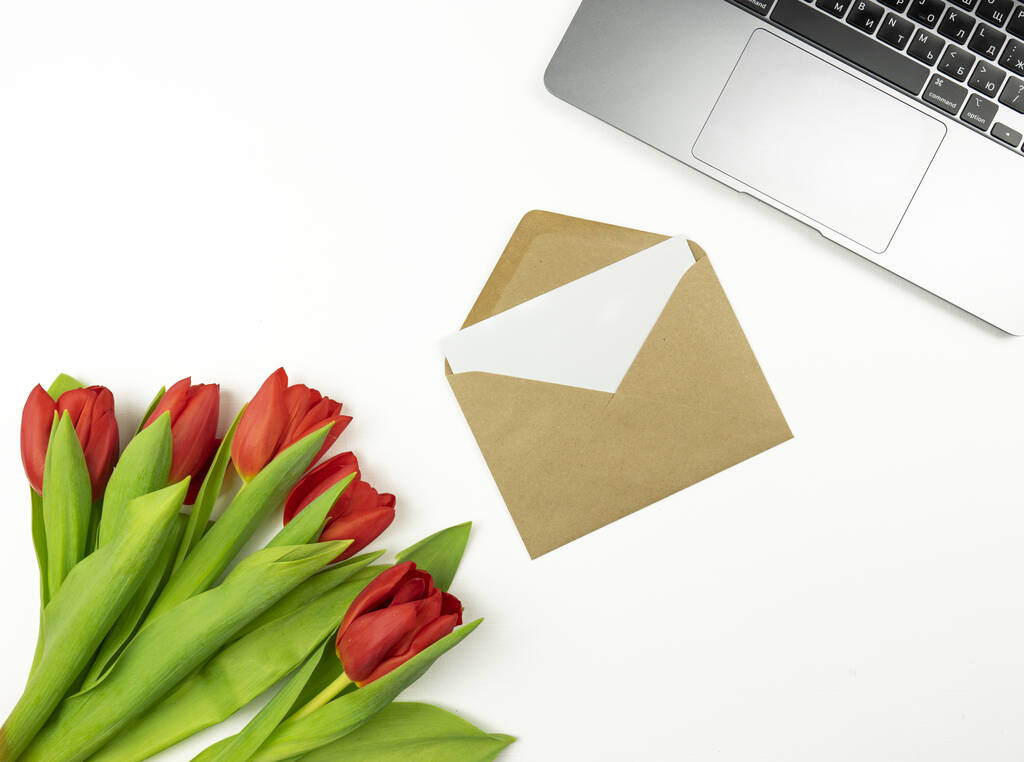 Red tulips and a blank letter in a brown envelope lie on a white table. Mockup - Photo, Image