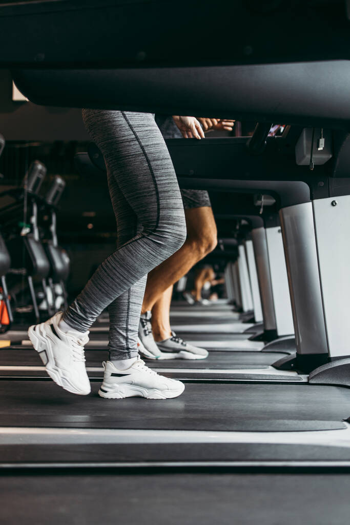 Young fit woman and man running on treadmill in modern fitness gym. Close up shot on moving legs. - Photo, Image