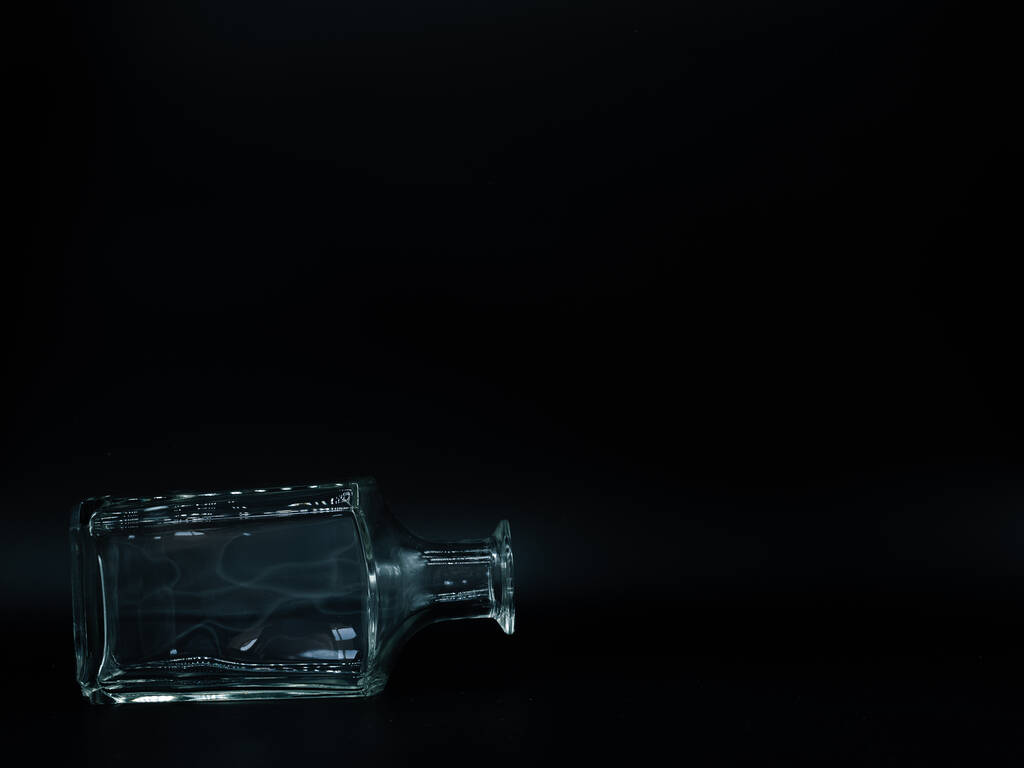 Одна порожня скляна пляшка на чорному тлі. Прозора квадратна пляшка. Передній вигляд кладки на його стороні прозора квадратна пляшка
. - Фото, зображення