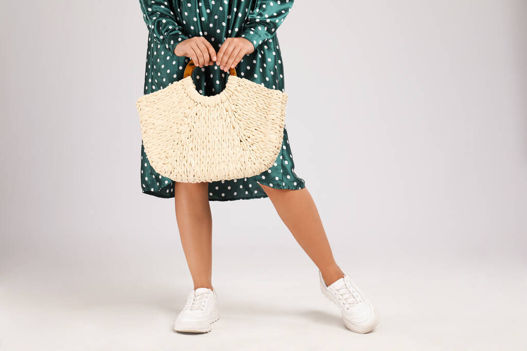 Молодая женщина со стильной соломенной сумкой на светло-сером фоне, крупным планом - Фото, изображение