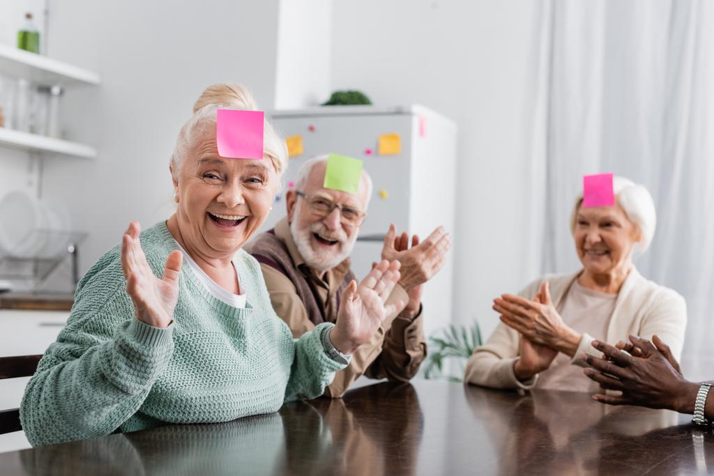 izgatott és multikulturális senior barátok ragadós jegyzetek homlokán játszik találd ki, ki a játék a konyhában  - Fotó, kép