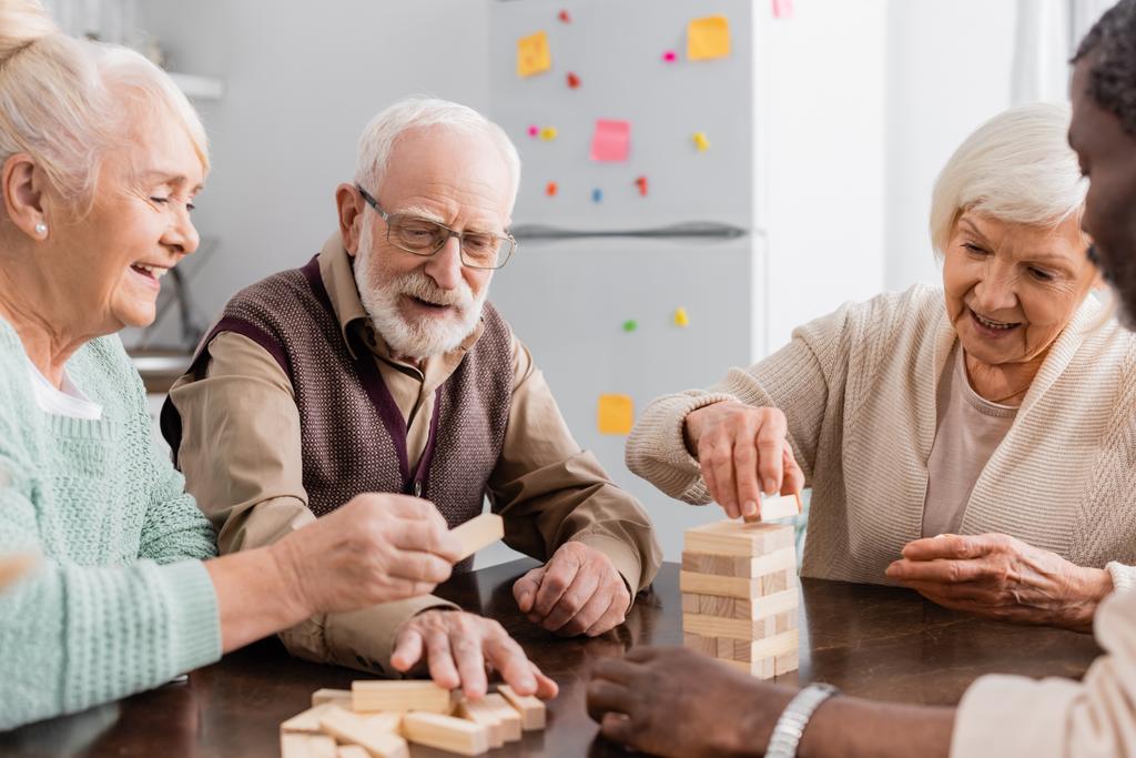 felici pensionati interrazziale sorridente durante la riproduzione di gioco blocchi di legno torre a casa - Foto, immagini
