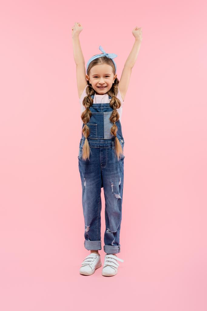 full length of happy kid standing with raised hands on pink - Photo, Image