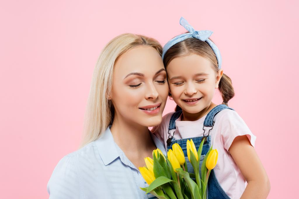 šťastná matka a dcera se zavřenýma očima usmívající se blízko tulipánů izolovaných na růžové  - Fotografie, Obrázek