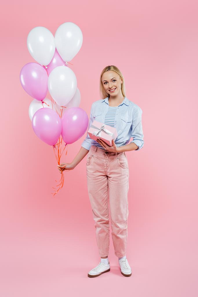 volle Länge der glücklichen Frau mit Luftballons und Geschenkbox auf rosa - Foto, Bild