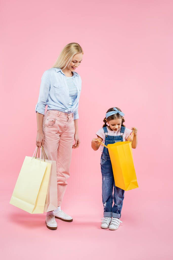 longitud completa de la madre y la hija alegre mirando el bolso de compras en rosa - Foto, imagen