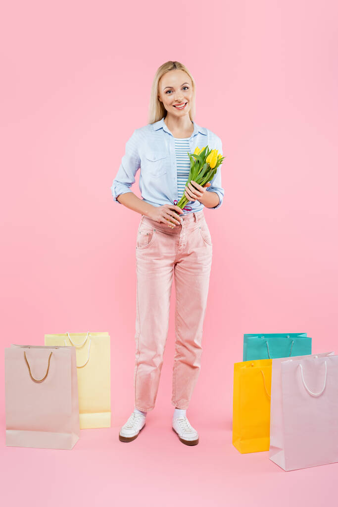 koko pituus onnellinen nainen tilalla keltainen tulppaanit lähellä ostoskassit vaaleanpunainen - Valokuva, kuva
