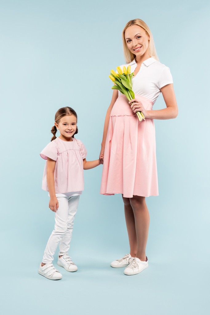 full length of kid holding hands with pregnant mother with tulips on blue - Photo, Image