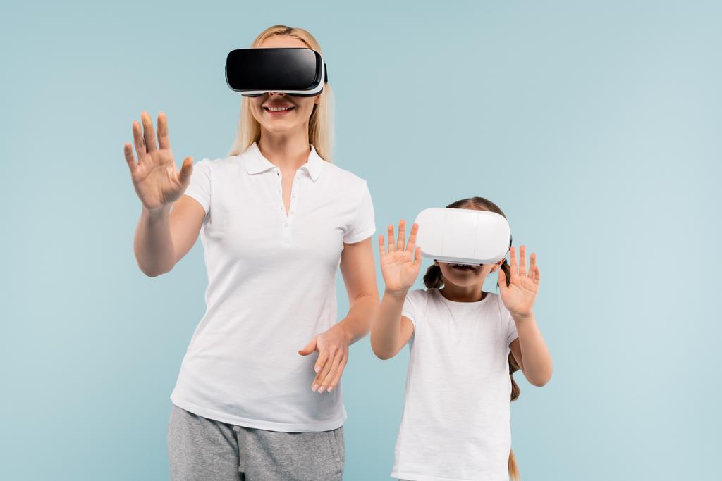 cheerful mother and kid in vr headsets gesturing isolated on blue - Photo, Image