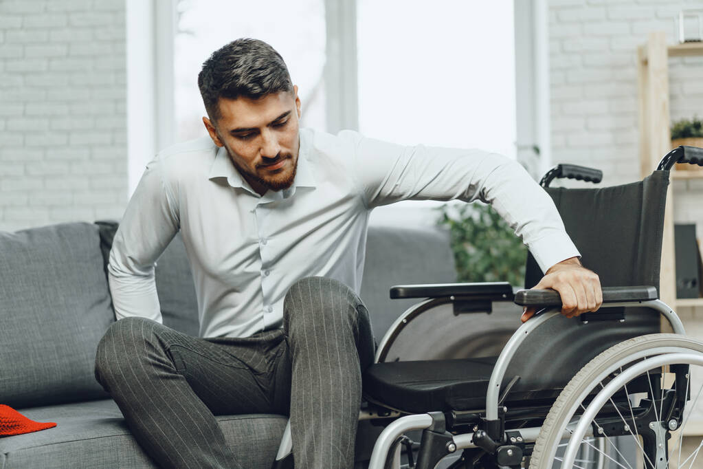 Uomo disabile cerca di sedersi su un divano da sedia a rotelle - Foto, immagini
