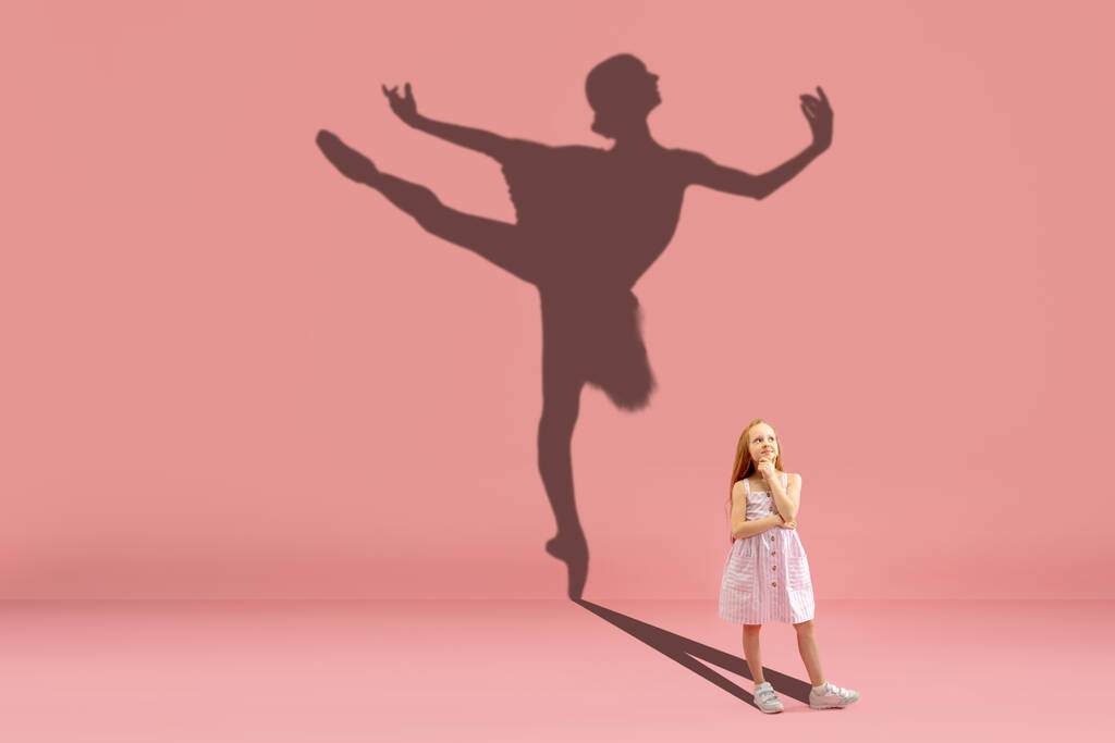 Infância e sonho sobre o futuro grande e famoso. Imagem conceitual com menina e sombra de bailarina fit dançando no fundo rosa coral - Foto, Imagem