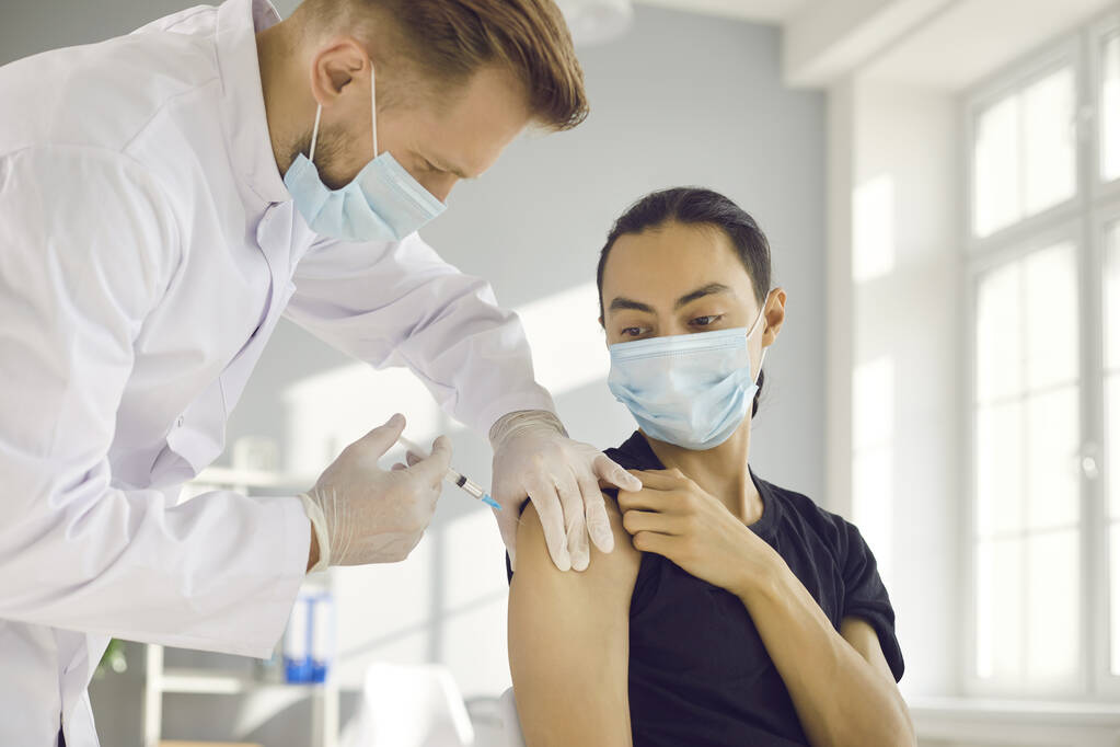 Молодий хлопець в масці для обличчя отримує вакцину під час кампанії з імунізації в медичному центрі
 - Фото, зображення