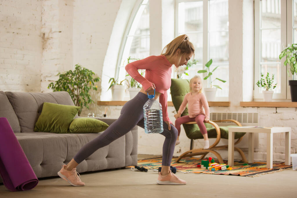 Mujer joven ejercitando fitness, aeróbico, yoga en casa, estilo de vida deportivo. Ponerse activa con su hijo jugando, gimnasio en casa. - Foto, imagen