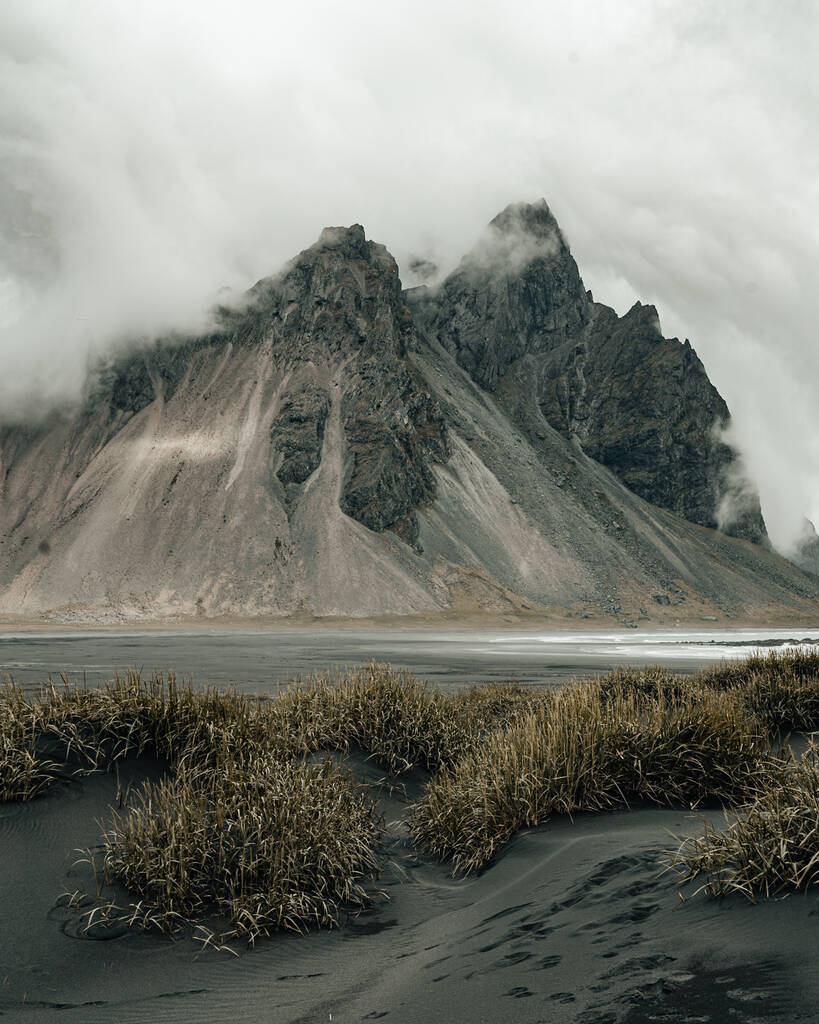 Un tiro vertical de la orilla con arena negra y montañas de arena en un clima brumoso en Islandia - Foto, Imagen