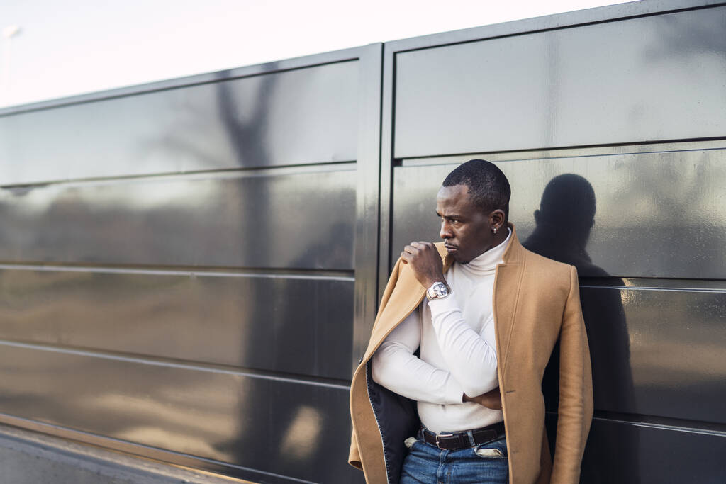 Una foto de enfoque superficial de un hombre africano guapo con estilo en un abrigo posando para la cámara - Foto, imagen
