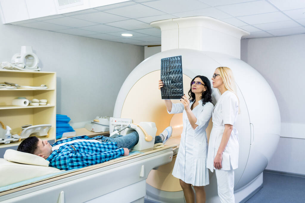 Radiologista com um paciente do sexo masculino examinando uma ressonância magnética - Foto, Imagem