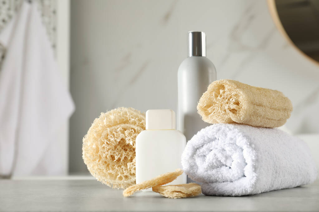 Esponjas de esponja natural, toalla y productos cosméticos en la mesa en el baño - Foto, Imagen
