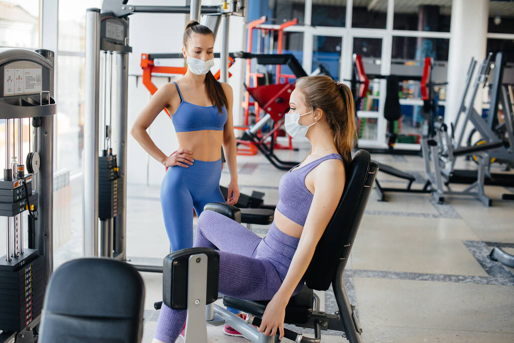 Deux jeunes filles magnifiques font de l'exercice dans la salle de gym portant des masques pendant la pandémie. Distance sociale dans les lieux publics. - Photo, image