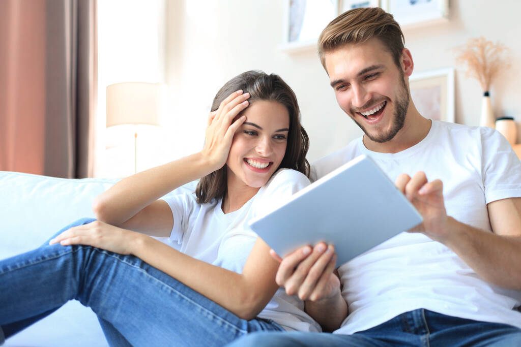 Mladý pár sledovat mediální obsah on-line v tabletu sedí na pohovce v obývacím pokoji - Fotografie, Obrázek