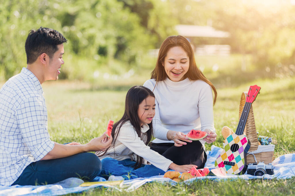 Onnellinen aasialainen nuori perhe isä, äiti ja lapsi pieni tyttö hauskaa ja nauttia ulkona istuu piknik huopa syö vesimeloni hedelmä välipala lounas puistossa aurinkoinen aika, kesä vapaa-ajan konsepti - Valokuva, kuva