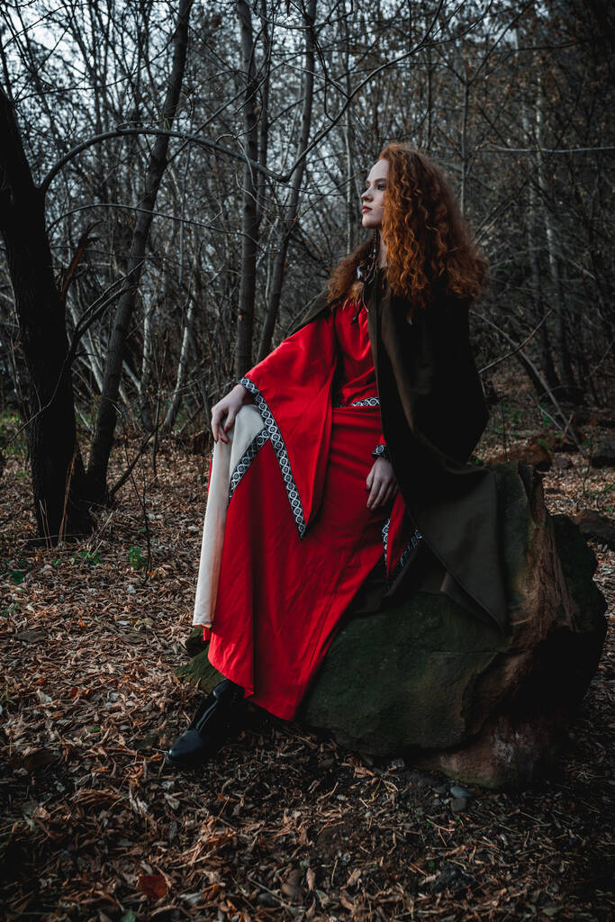 Mujer pelirroja con un vestido rojo en un traje histórico celta en el bosque de otoño - Foto, imagen