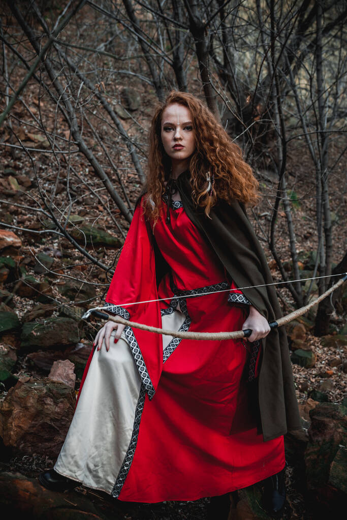 Rudowłosa kobieta w czerwonej sukience w historycznym celtyckim kostiumie w jesiennym lesie - Zdjęcie, obraz