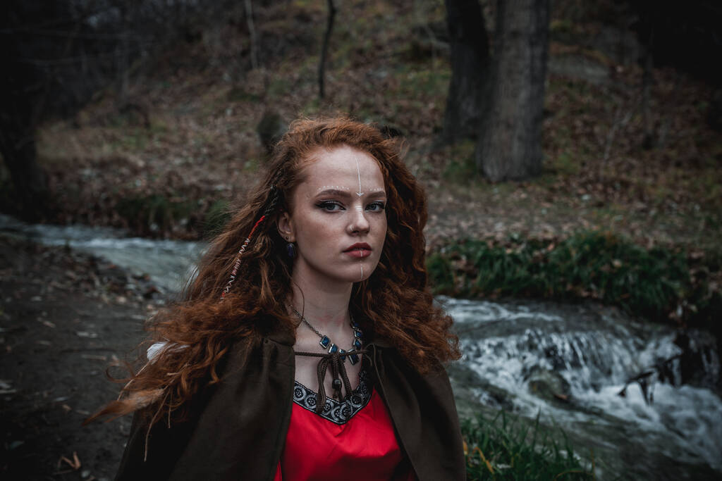 Rudowłosa kobieta w czerwonej sukience w historycznym celtyckim kostiumie w jesiennym lesie - Zdjęcie, obraz