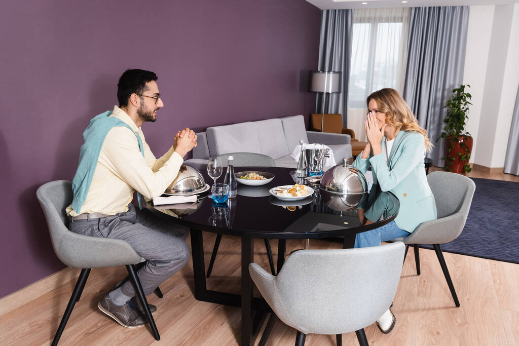 Μουσουλμάνος άνδρας που ψάχνει κοπέλα κοντά σε νόστιμο δείπνο στο δωμάτιο του ξενοδοχείου  - Φωτογραφία, εικόνα