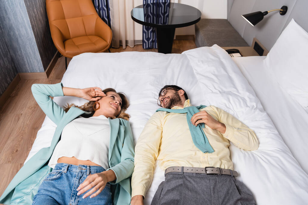 Alto ángulo de vista de la sonrisa interracial pareja acostada en la cama en el hotel  - Foto, Imagen