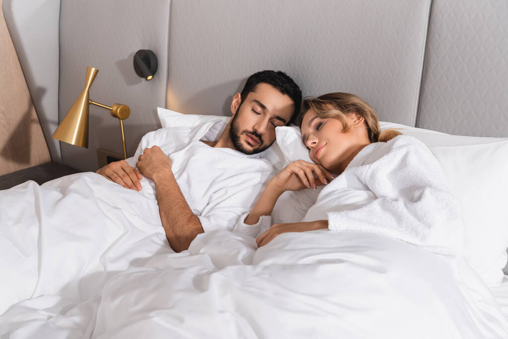 Young interracial couple sleeping on white bedding in hotel  - Photo, Image
