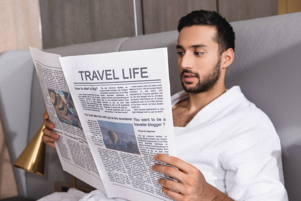 Travel life lettering on newspaper in hands of arabian man in bathrobe in hotel  - Photo, Image