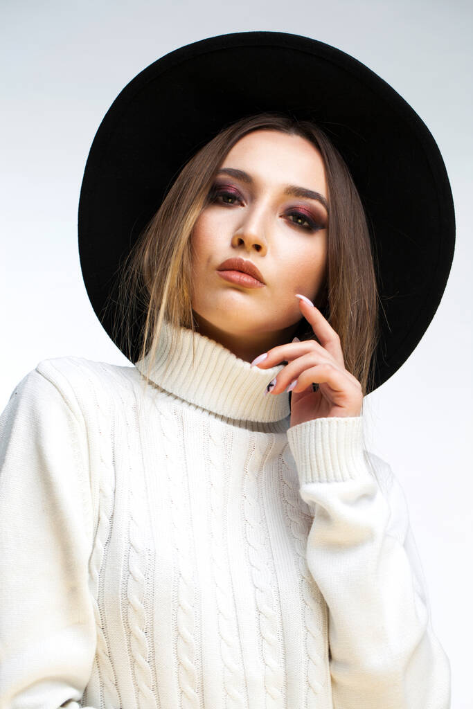 Maquillaje. Retrato de una joven con estilo en un sombrero negro y suéter blanco - Foto, imagen