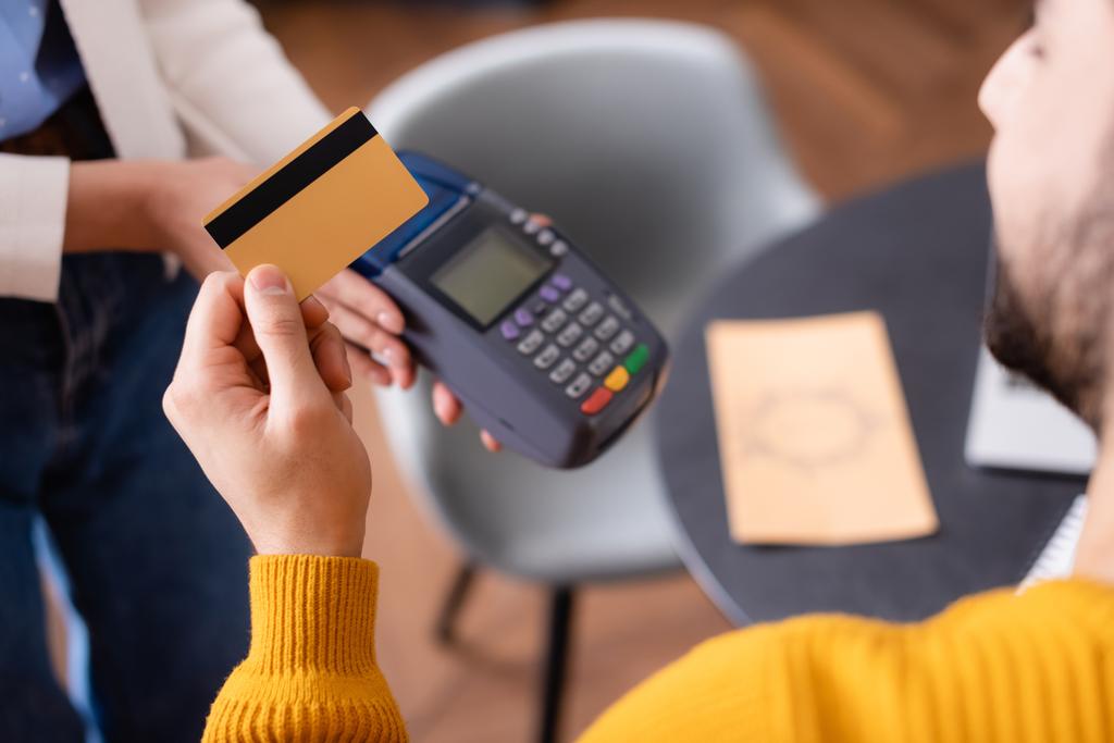 gedeeltelijk zicht op Arabische man houden credit card in de buurt van betaalterminal in handen van serveerster - Foto, afbeelding