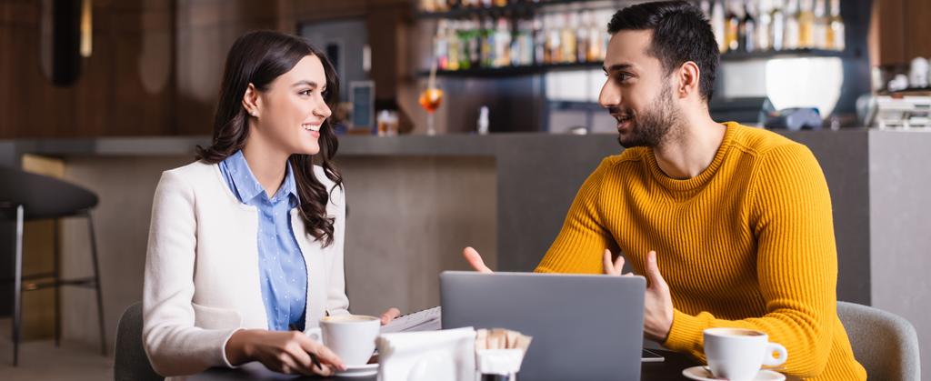 freelancer árabe falando com amigo sorridente perto de laptop no restaurante, foreground borrado, banner - Foto, Imagem