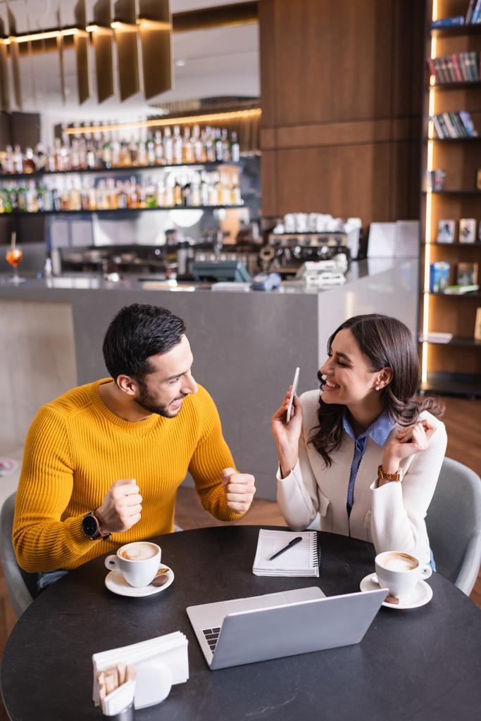 Arabský muž ukazuje ano gesto blízký přítel s chytrým telefonem, notebookem a kávou v restauraci  - Fotografie, Obrázek